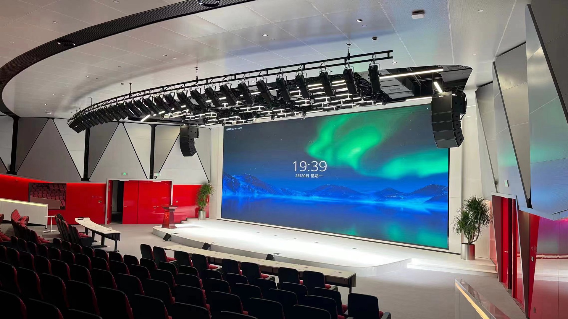 Suspended loudspeaker arrays flank the stage in a corporate auditorium.